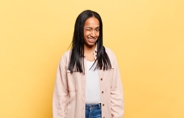 young black woman looking happy and friendly, smiling and winking an eye at you with a positive...
