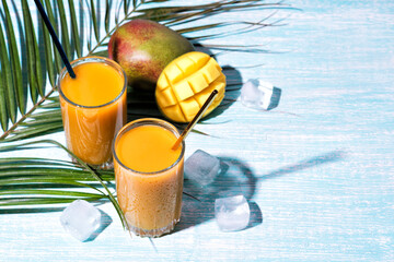 Glass of fresh mango juice cocktail and palm branches blowing in the wind. Vertical video. Blue...