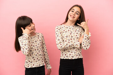 Little sisters girls isolated on pink background making phone gesture. Call me back sign