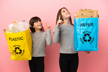 Little sisters recycling paper and plastic isolated on pink background pointing with the index finger a great idea