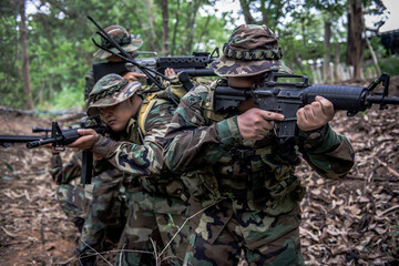 Fototapeta premium Team of army soldier with machine gun moving in the forest,Thai militia soldier in combat uniforms in the wood,Wander the patrol sloping in the rainforest.