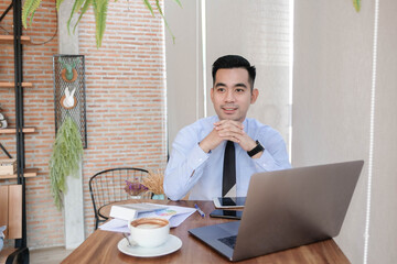 Young asian business man working with laptop, tablet and papers on desk at office. He feeling good and happy.