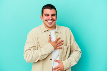 Young caucasian man isolated on blue background laughs happily and has fun keeping hands on stomach.