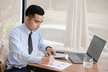 Young asian business man working with laptop, tablet and papers on desk at office.