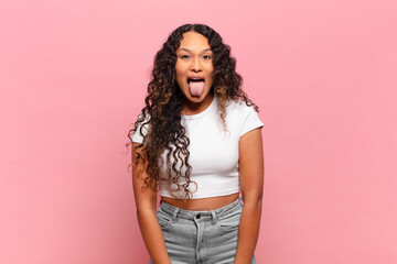 young hispanic woman with cheerful, carefree, rebellious attitude, joking and sticking tongue out,...