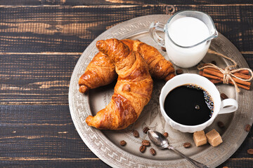 Croissant with chocolate hazelnut spread and cup of coffee on a metal vintage tray. Continental breakfast with flowers on dark wooden table