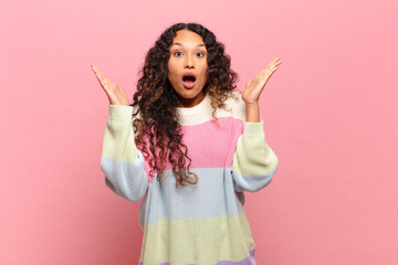 young hispanic woman looking shocked and astonished, with jaw dropped in surprise when realizing...