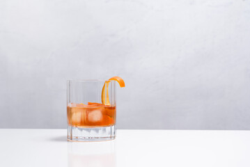 Vaso de vermú rojo decorado con una rodaja de naranja y hielo sobre mesa blanca