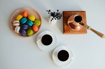 Two cup of coffee, multicolored macaroons, turkish coffee pot on white background, top view