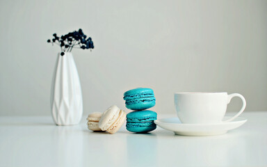 White cup of coffee, multicolored macaroons, vase with a sprig of dried berries on white background, close up