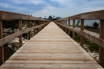 Close-up of empty wooden boardwalk and handrail over grassy dune and blue cloudy sky at Lagoa da Vela, Portugal. The way ahead concept