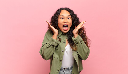young hispanic woman feeling shocked and excited, laughing, amazed and happy because of an...