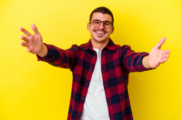 Young caucasian cool man isolated on yellow background feels confident giving a hug to the camera.