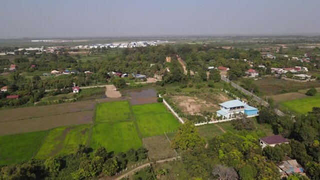 Aeria footage in the nearby countryside near Phnom Penh city the capital of Cambodia. Mix of green fieds and trees and new construction in the background