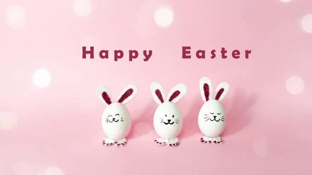 4k Happy Easter Day Concept. Three eggs turn and transformation into Easter bunnies and congratulate on the holiday. Light pink background. Greeting card with bokeh. Stop motion animation. Copy space.