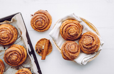Freshly baked homemade cinnamon rolls in basket and on oven pan in the morning indoors, breakfast...