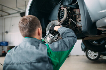 Car lifted in automobile service for fixing, worker repairs the wheel,