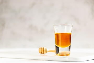 Honey shot and wooden dipper on marble tray with light gray background and copy space. 