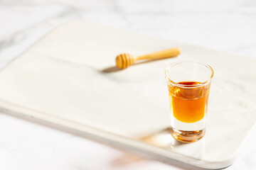 Honey shot and wooden dipper on marble tray with light gray background and copy space. 