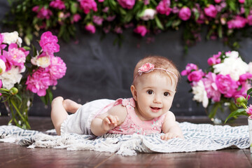Obraz na płótnie Canvas Portrait of a beautiful little baby girl with pink flowers. Sweet smiling girl lying on her stomach