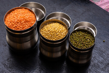 Three jars full of mung dal, green mung and munsuri dal three types of lintel on a black wooden table.
