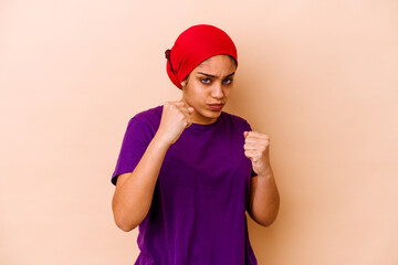 Young african american woman isolated on beige background throwing a punch, anger, fighting due to an argument, boxing.
