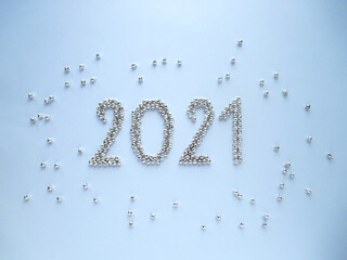 2021 on a gray background. View from above. A year in the middle. Small silvery bells are scattered throughout the background. 2021 is made of metal silver bells. New Year. Christmas.           