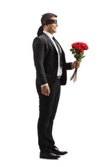 Full length profile shot of a man in a suit with blindfold holding a bunch of red roses