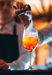 Barman hand stirring a fresh and sweet orange summer cocktail with a spoon on the bar counter.
