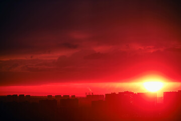 Setting evening sun behind the silhouettes of buildings. Nightfall in the big city. Top view of the city at dusk