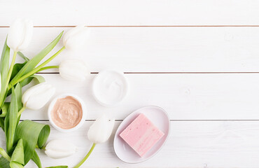 Top view of cosmetic creams and soap with white tulips top view flat lay on white wooden background