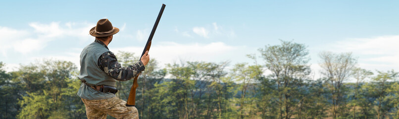 A hunter with a gun in his hands in hunting clothes in the autumn forest in search of a trophy. A...