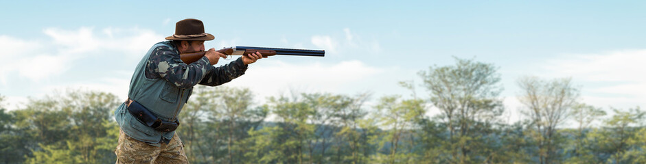 A hunter with a gun in his hands in hunting clothes in the autumn forest in search of a trophy. A man stands with weapons and hunting dogs tracking down the game.