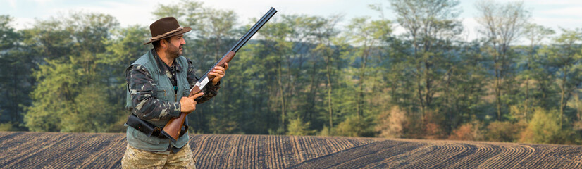 A hunter with a gun in his hands in hunting clothes in the autumn forest in search of a trophy. A...