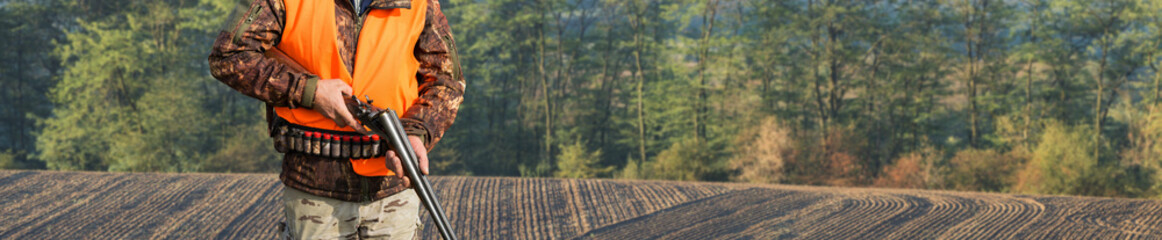A hunter with a gun in his hands in hunting clothes in the autumn forest in search of a trophy. A...