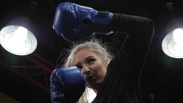 A beautiful young active woman trains in a boxing ring, she practices punches.