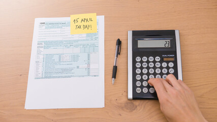 Filling 1040 form on tax day with calculator on table to be returned. American event.