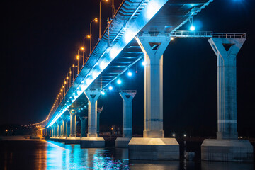 Side view of colourful bridge illuminated with blue color lights at the night. Bridge stands on Volga river in Russia. Blue light is reflected in the water.