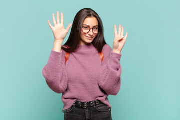 young pretty woman smiling and looking friendly, showing number nine or ninth with hand forward,...
