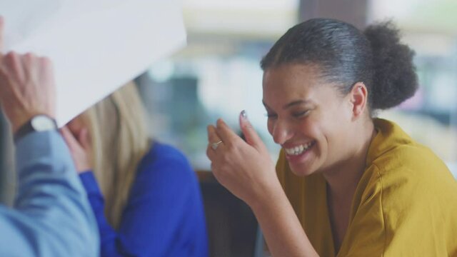 Close up of laughing businesswomen sitting around table in office having informal discussion - shot in slow motion