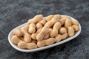 Shelled peanuts on plate on dark background