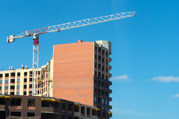 Fototapeta na wymiar Urban housing construction. A crane and a house under construction on a blue sky background. Purchase of apartments in buildings under construction. Mortgage, business, real estate loan.