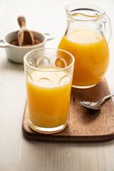 Top view of glass and jug with orange juice, spoon, and brown sugar, on white wood, in vertical