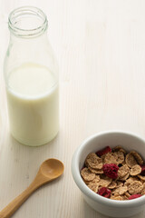 Top view of cereal bowl, milk bottle and wooden spoon, on white wooden table, in vertical, with copy space