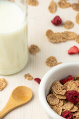 Close-up of cereal bowl, milk bottle and wooden spoon, on white wooden table, in vertical