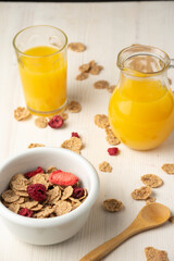 Top view of cereal bowl, spoon, jug and glass with orange juice, on white table, in vertical