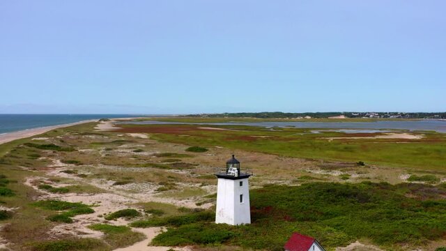 Aerial panning shot of lighthouse at beach against blue sky on sunny day, drone flying forward over coastline - Cape Cod, Massachusetts