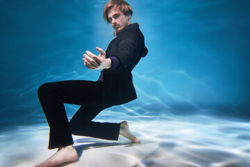 Young european guy swims underwater in the pool wearing clothes