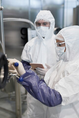 Side view at two workers wearing protective suits while using machines at modern chemical plant
