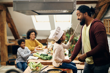 Playful black girl and her father having fun while preparing food in the kitchen.